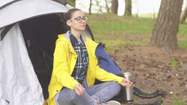 Genç turist kadın bir çadırın yanında oturur ve ormanda meditasyon yapar.