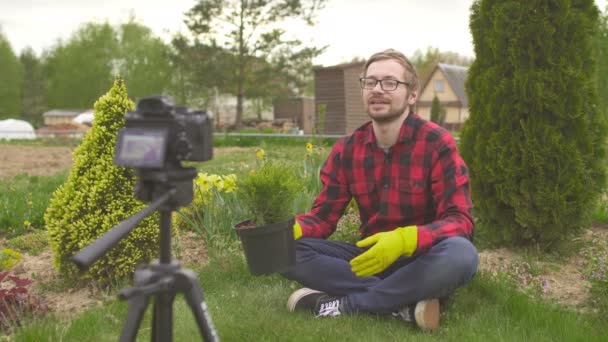 Joven blogger jardinero sosteniendo enebro de coníferas hablando con la cámara — Vídeo de stock