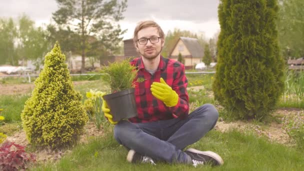 Jovem blogueiro jardineiro segurando planta conífera e falando com a câmera — Vídeo de Stock