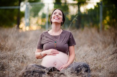 happy young pregnant woman smiling sitting down on the fields. clipart