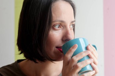 Genç, doğal, güzel bir kadın, huzurlu ve mutlu bir ifadeyle rahat bir sabahta evde kahve içiyor..