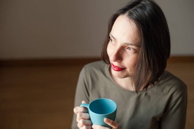 Genç, doğal, güzel bir kadın, huzurlu ve mutlu bir ifadeyle rahat bir sabahta evde kahve içiyor..