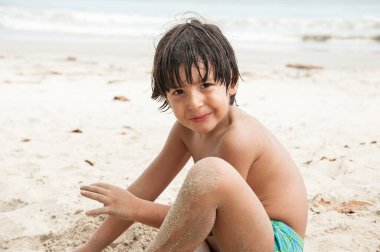 Genç bir çocuk, bulutlu bir günde kumsalda tek başına oynarken eğleniyor. Lagoinha Sahili, Ubatuba, SP, Brezilya