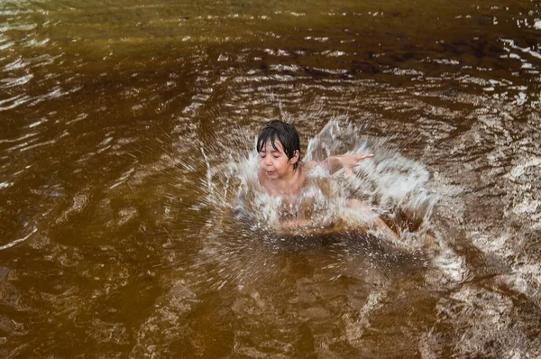 young brazilian child jumping at the river splashing water everywhere