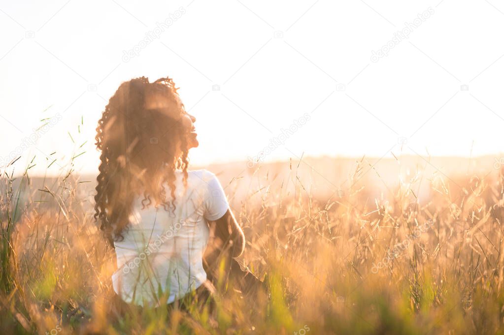 afro american girl on her back sitting in the field at sunse