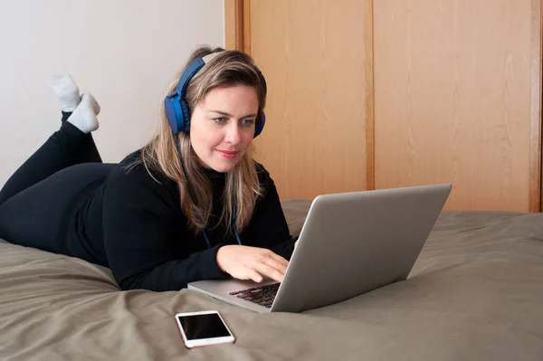 침대에서 컴퓨터를 사용하는 여성의 헤드폰을 있어요 — 스톡 사진