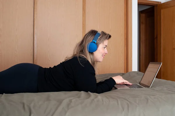 Blonde Vrouw Met Behulp Van Computer Bed Gebruikt Een Koptelefoon — Stockfoto