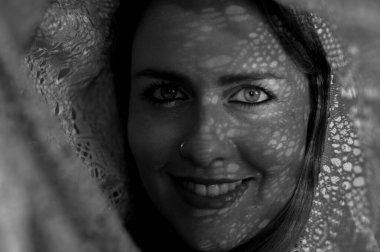 Genç sarışın kadın kameraya bakıyor. Yüzüne gölgeler yansıtıyor..