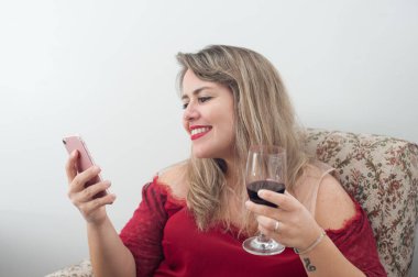 Günlük hayat sahnesi. Evde cep telefonu kullanan ve şarap içen genç sarışın kadın..