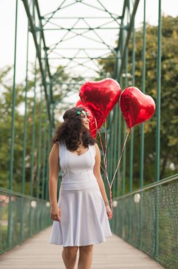 Romantik bir sahne. Parkta yürüyen kız kalp şeklinde kırmızı balonlar taşıyor..