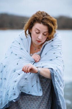 Battaniyeye sarılı bir kız saatine bakar.