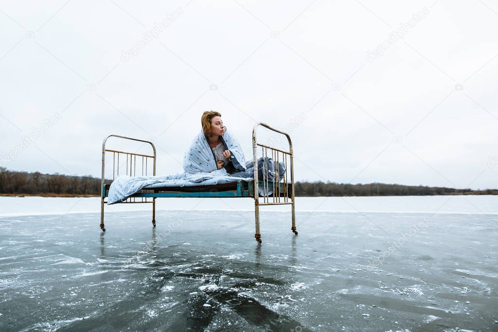 A girl in a nightgown and a blanket , waking up on a bed on a frozen blue lake