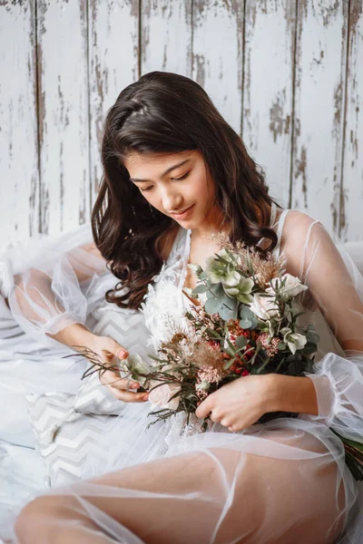 Asian bride in underwear with wedding bouquet, on the bed