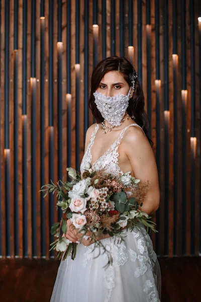 Bride in with a handmade wedding antiviral mask on her face. Wedding bouquet in hand