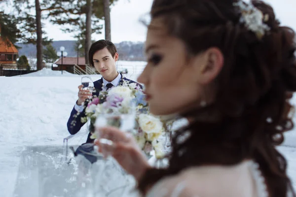The bride and groom are sitting at a glass table on the street. Winter, snow around