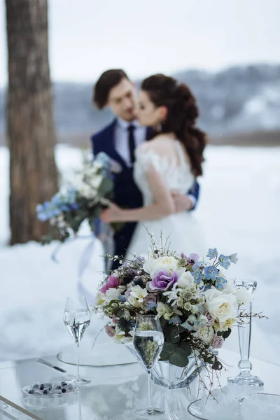 新郎新婦の背景にガラステーブルの上に結婚式の花 冬の結婚式の撮影 — ストック写真