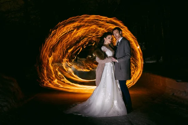新郎は炎の背景に花嫁を包含し 雪の中に立っている 光と光の絵画を凍結することによる夜の写真の技術 — ストック写真