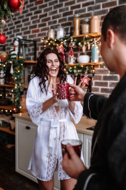 Mutfaktaki sabahlıklı insanlar Noel için dekore edilmiş. Adam kıza bir fincan kakao ikram ediyor.