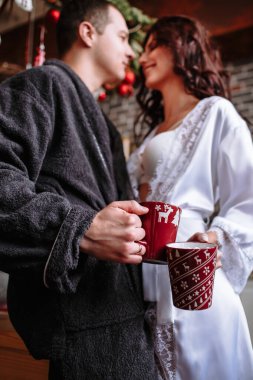 İnsanlar Noel için dekore edilmiş bornozlarını mutfakta giyiyor. Bir erkek ve bir kızın ellerinde. Kakaolu ve şekerli kupalar.