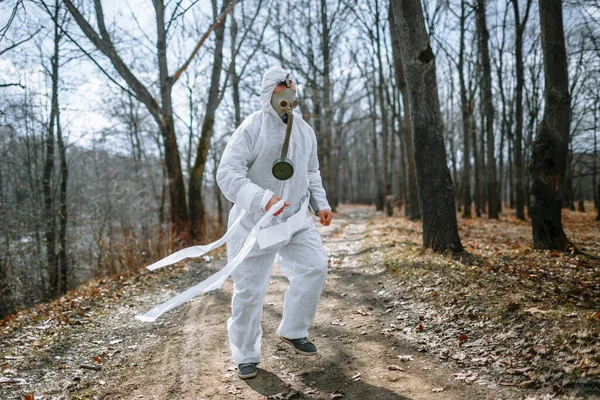 A man in a sanitary suit and a gas mask is Jogging in the woods. The suit is tied with toilet paper