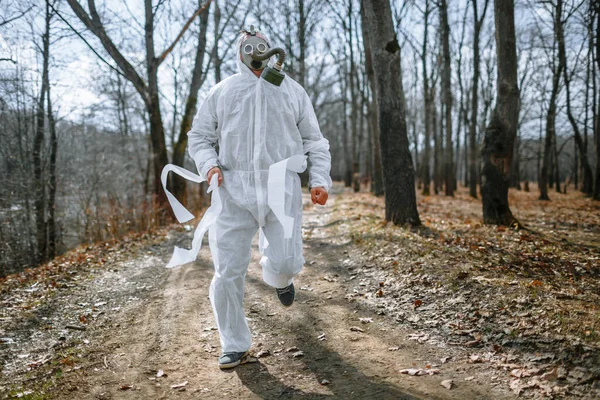 A man in a sanitary suit and a gas mask is Jogging in the woods. The suit is tied with toilet paper