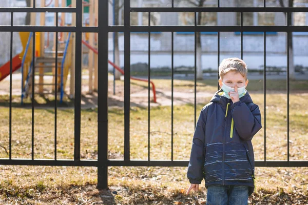 A boy in a medical mask makes a Shhh gesture