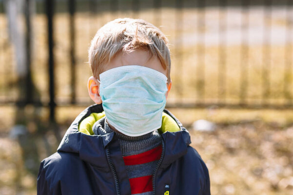 Next to a metal fence stands a boy in a medical mask that covers his face completely