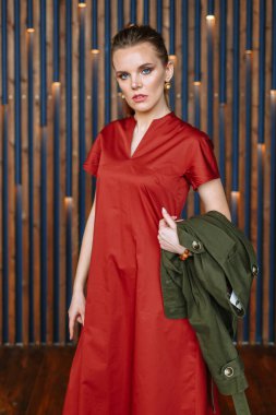 Kırmızı elbiseli ve yeşil ceketli manken kız. Galeri için kıyafet gösterisi.