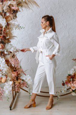 Açık beyaz bir yaz elbisesi içindeki model kız bir çiçek kemerinin arka planında. Galeri için kıyafet gösterisi.
