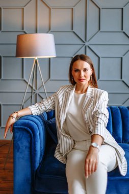 Mavi bir kanepede takım elbiseli model bir kız. Galeride kıyafet gösterisi..