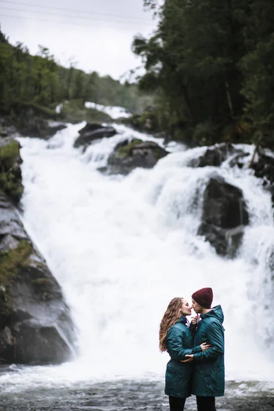 滝を背景にした緑のレインコート姿の恋人像 — ストック写真