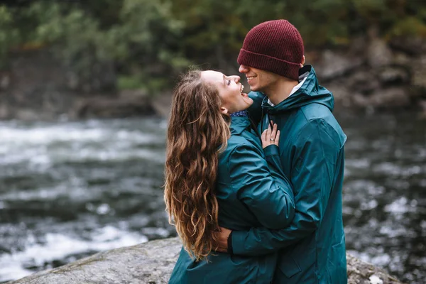 在挪威瀑布的背景下 恋人身穿绿色雨衣 表现爱情情调的画像 — 图库照片