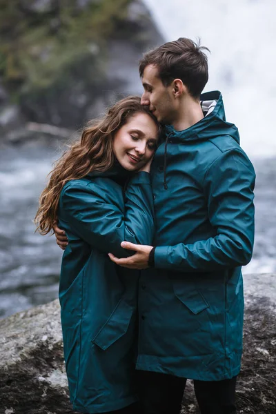 Bir Şelalenin Arka Planında Duran Yeşil Yağmurluklu Sevgililerin Portresi — Stok fotoğraf