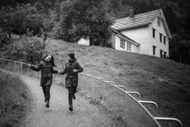 Yağmurluklu âşıkların küçük bir tepeden aşağı koştuğu siyah beyaz bir fotoğraf.