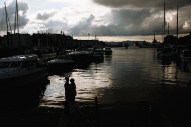 Bergen şehrinde yatları olan küçük bir limanın arka planında iki aşığın siluetleri