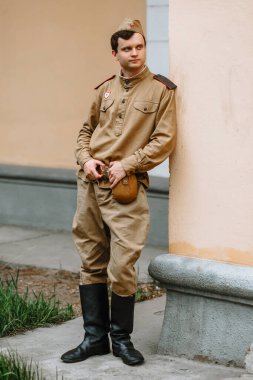 II. Dünya Savaşı 'ndan kalma Sovyet üniformalı bir adam. Asker sarı duvara karşı duruyor, elleriyle kemerini tutuyor. Ciddi yüz.