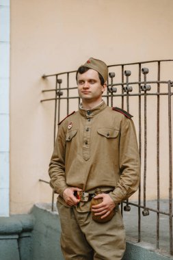 II. Dünya Savaşı 'ndan kalma Sovyet üniformalı bir adam. Asker sarı duvara karşı duruyor, elleriyle kemerini tutuyor. Ciddi yüz.