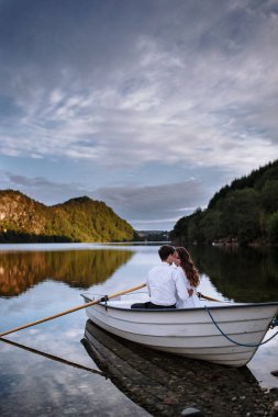 Düğün çifti gölde bir teknede oturup sarılıyorlar.