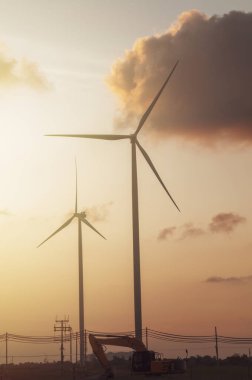 Rüzgar türbinleri ve güç hattı olan kazıcı. Güneş, elektrik üretmek için kullanılan rüzgar türbininin arkasında. Yenilenebilir Enerji Kavramları ve Dünya Enerjisini Korumaya Yardım Edin