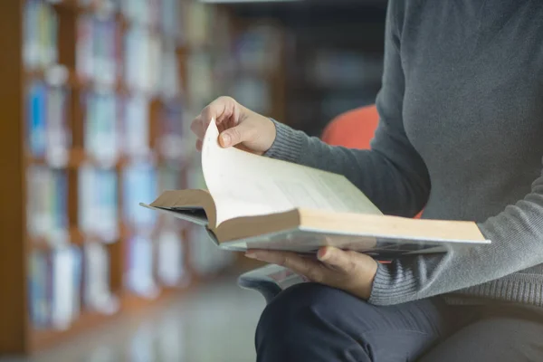 Üniversite kütüphanesinde kitabı açıp okuyan yakın plan bir kadın. Eğitim öğrenme kavramı.