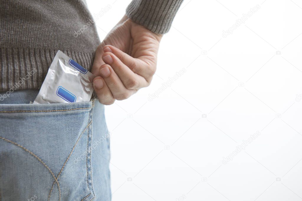 Young man jeans back side pocket to carry condoms taking in hand condom from jeans isolated on white background, safe sex concept on the bed Prevent infection.