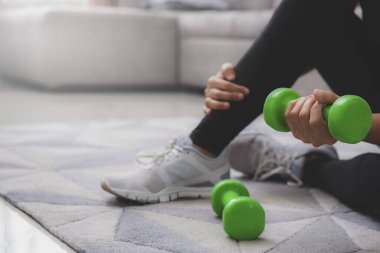 Spor giyim sektöründe sportif bir kadın dambıllarıyla yerde oturuyor. Spor ve eğlence konsepti. Coronavirus önleme kampanyası için evinizde kalın.