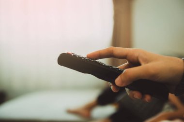 Evdeki kanepede otururken uzaktan kumandayı elinde tutan ve televizyonu açan genç bir kadının yakın çekimi. Virüsü durdur Covid-19. Evde kal..