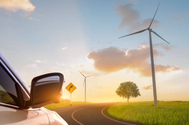 Yeşil enerji konsepti. Rüzgar türbinleri ve günbatımı arka planlarıyla yeşil alanda yol.