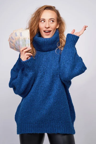 Радостная женщина в свитере, счастливая с деньгами гривны, держа их — стоковое фото