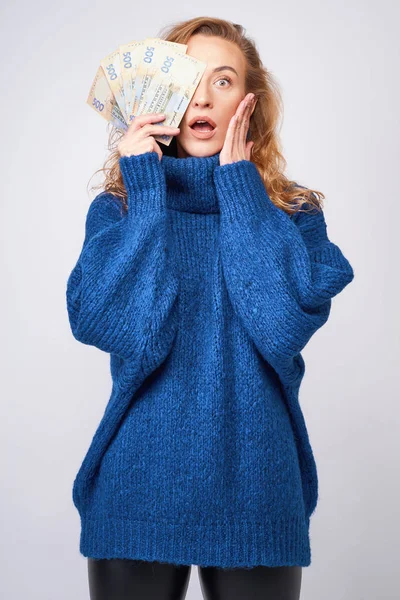 Young woman in a sweater is surprised by money, on a gray backgr — Stock Photo, Image