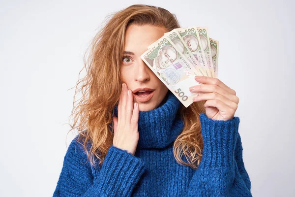 Young woman in a sweater is surprised by money, on a gray backgr — Stock Photo, Image