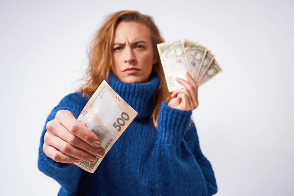 Разочарованная девушка в свитере, держащая деньги на серой бэкгру — стоковое фото