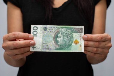 PLN 100 Polonya parası değerindeki bir banknotun kapanışı. Gri arka plandaki bir kadının elinde zloti.