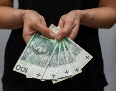 PLN 100 Polonya parası değerindeki bir banknotun kapanışı. Gri arka plandaki bir kadının elinde zloti.